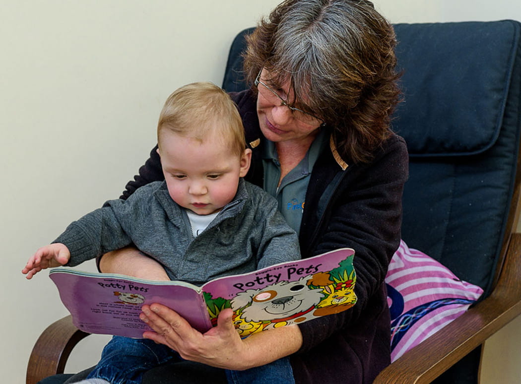 First Grammar learning program, day care educator reading to a baby